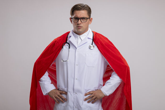 外套超级英雄医生男人身穿白色外套 披着红色斗篷 戴着眼镜 脖子上戴着听诊器 表情严肃自信地看着镜头 手臂放在臀部 站在白色背景上超级眼镜超级英雄