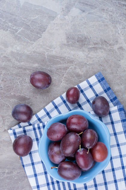 新鲜用桌布在石头背景上放一碗新鲜的李子紫色美味水果