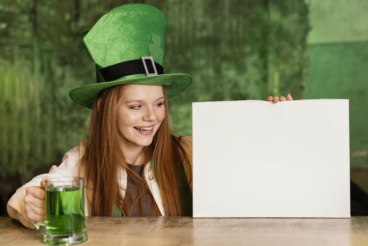 绿色笑脸女人庆祝圣帕特里克节在酒吧与空白标语牌和饮料帽子酒吧女士
