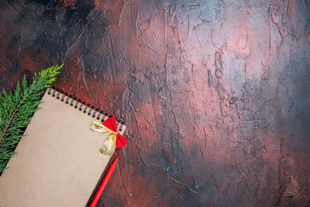 底顶视图红色钢笔一个小蝴蝶结的记事本一个松树枝在暗红色的表面左下角有复印空间小古董视图