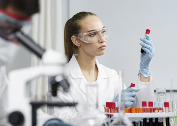 水平实验室里的女研究员拿着试管和安全眼镜 旁边是男同事试管显微镜开拓者
