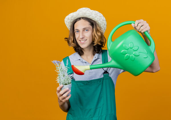 欢呼年轻的园丁 穿着连体衣 戴着帽子 手里拿着水罐和盆栽植物浇水植物举行