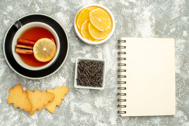 笔记本顶视图一杯茶 柠檬片和肉桂棒饼干碗巧克力笔记本在灰色表面顶部茶巧克力