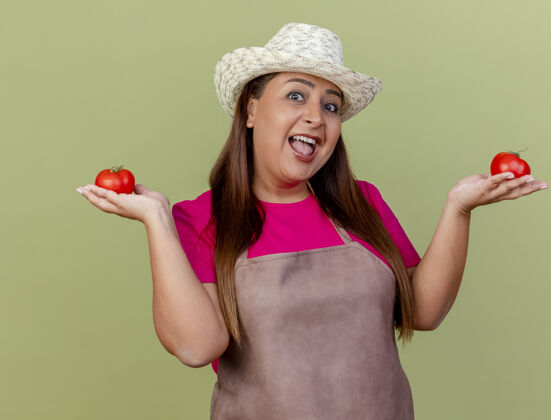 脸穿着围裙 戴着帽子 手里拿着新鲜西红柿的快乐的中年园丁女人花园光围裙