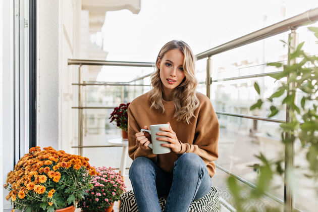 情绪可爱的欧洲女人在露台上喝茶有兴趣的金发女孩在喝咖啡的画像欢笑假期享受