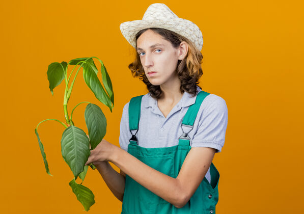 花园年轻的园丁穿着连体衣戴着帽子拿着植物连身衣男人脸