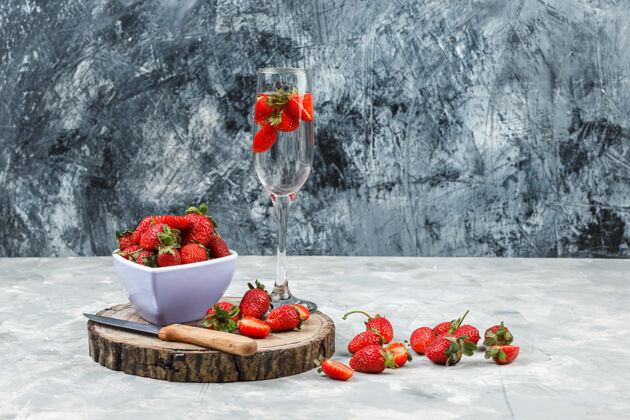 树叶把一碗草莓放在木板上 一杯饮料放在白色和深蓝色大理石表面水平生的维生素水果