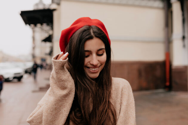 自信浪漫害羞的女人 留着长长的黑头发 戴着红帽子和米色夹克 走在街上大笑人表情