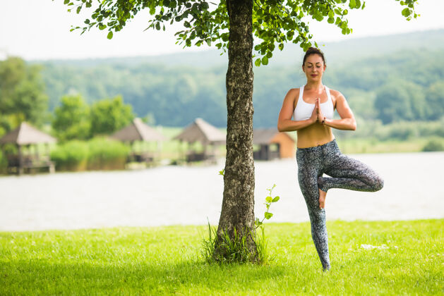 树木年轻健康的女人在湖边和树边的公园里做瑜伽度假村人放松