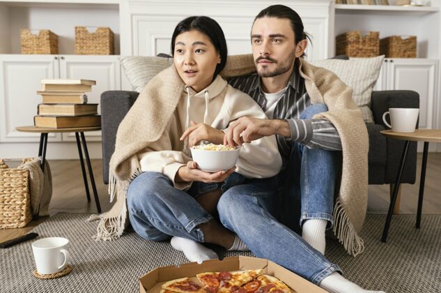 看电视一对穿着毛毯看电影吃东西的夫妇享受无忧无虑年轻