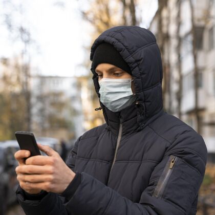 新常态带着医用面罩的男人在户外使用智能手机防护大流行人