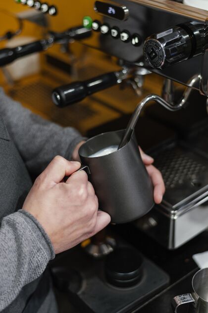 男性男咖啡师为咖啡准备牛奶泡沫的侧视图咖啡店垂直工作