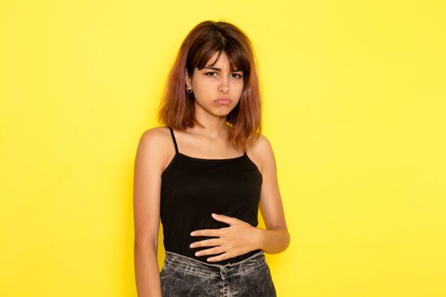 女孩身穿黑色衬衫的年轻女性在浅黄色墙壁上摆出悲伤表情的正面图工作表情模特