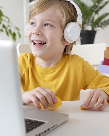垂直笑脸男孩使用笔记本电脑和耳机在家里孩子电子娱乐