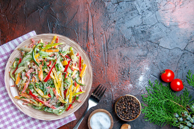 大蒜顶视图蔬菜沙拉放在盘子上桌布叉子上盐和黑胡椒大蒜西红柿放在深红色桌子上自由空间蔬菜沙拉料理餐厅