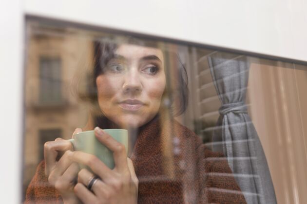 斯堪的纳维亚风格一个女人拿着一杯咖啡看着外面舒适生活方式女性
