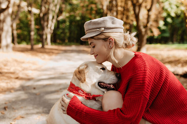 可爱在秋天的公园里 年轻的金发女郎穿着时髦的红色衣服对着她可爱的拉布拉多犬微笑可爱的女孩和她的狗在户外放松公园户外活跃