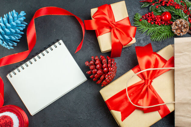 圣诞一卷红丝带针叶树球果和礼品冷杉树枝的水平视图 旁边是黑色背景上的笔记本视图蝴蝶结卷轴