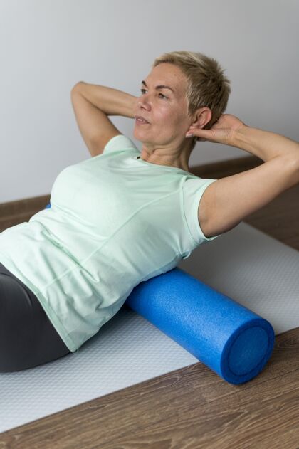 健康一位留着短发的高级女士正在使用瑜伽垫运动私人教练室内