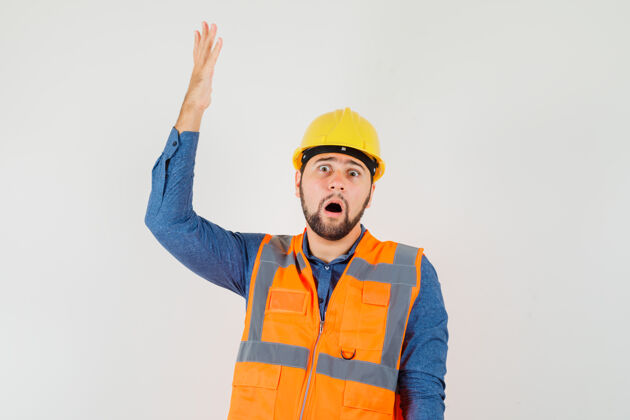 人年轻的建筑工人穿着衬衫 背心 头盔举起手 看起来很震惊 正面视图专业背心建筑工人