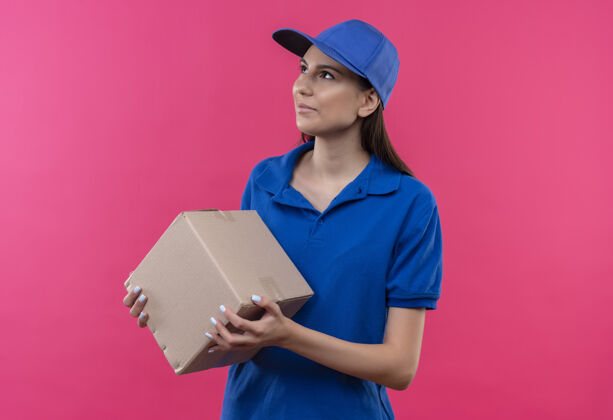 靠边穿着蓝色制服 戴着帽子的年轻送货女抱着盒子 严肃地看着一旁帽子女孩年轻