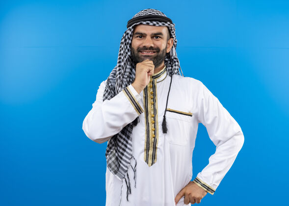 脸身着传统服装的阿拉伯男人 脸上带着微笑 站在蓝色的墙上 积极而快乐传统看积极