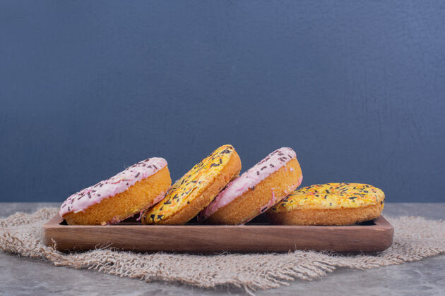 香草粉红色和黄色奶油甜甜圈放在木盘上面包房美味甜点