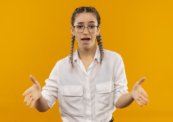站着一个戴着眼镜 梳着辫子 穿着白衬衫的年轻女学生站在橘色的墙上 看上去很困惑 很焦虑学生困惑非常