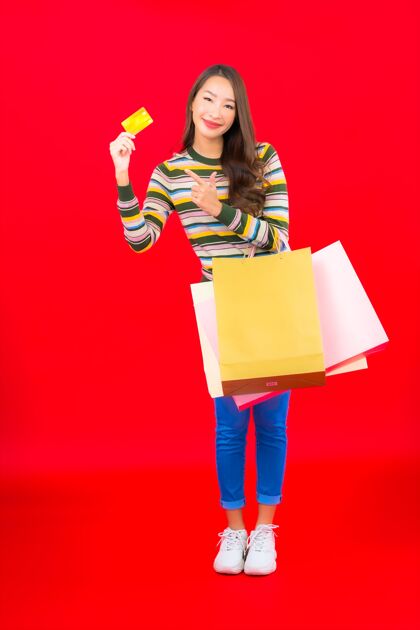 魅力在红墙上画一幅美丽的亚洲年轻女子的画像 上面有五颜六色的购物袋和信用卡时尚包买家