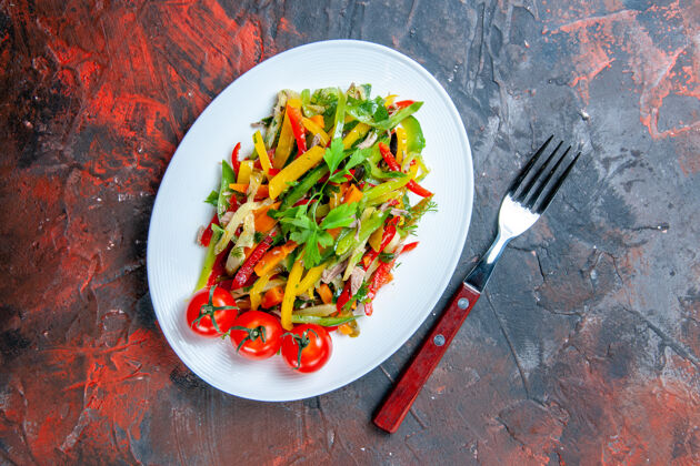 膳食俯视图蔬菜沙拉在椭圆形的盘子叉在暗红色的桌子上菜肴辣椒胡椒