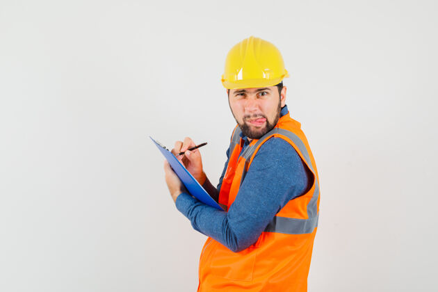 职业穿着衬衫 背心 头盔的年轻建筑工人在剪贴板上做笔记工程师头盔工作