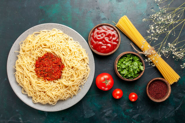 面食俯视图：深蓝色表面上有肉末番茄酱和调味料的意大利熟面食烹饪菜肴肉