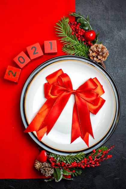 冷杉新年背景立面图 餐盘上有红丝带装饰配件杉木树枝 黑色桌子上有红色餐巾上的数字风景玫瑰圣诞