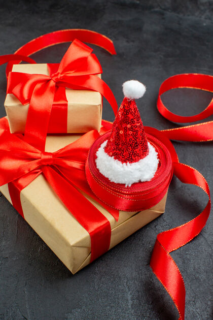 视图红色丝带和圣诞老人帽子在黑暗背景下的美丽礼物的垂直视图蝴蝶结包装圣诞老人