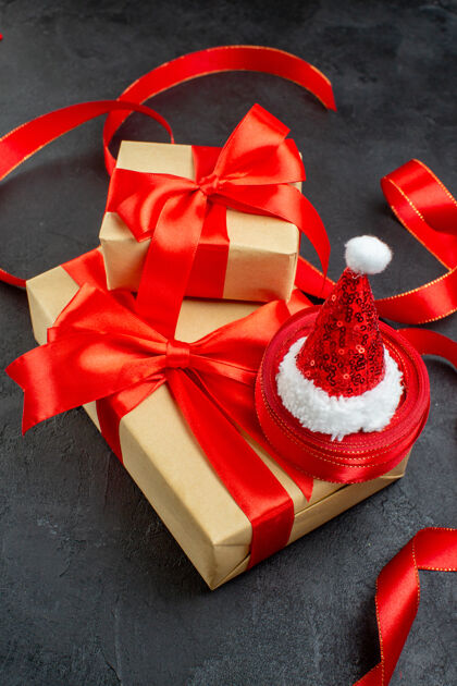 圣诞节黑色桌子上戴着红丝带和圣诞老人帽子的漂亮礼物的垂直视图轮子风景圣诞老人