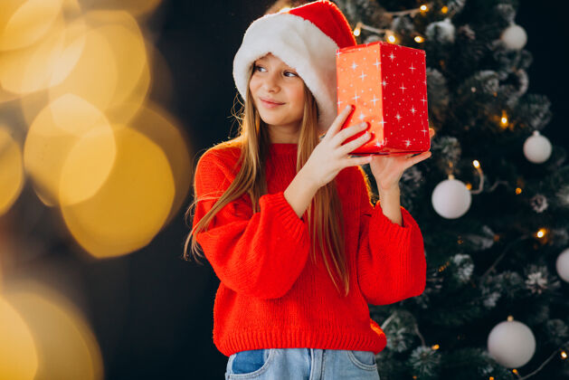 微笑可爱的少女戴着圣诞树旁的红色圣诞帽女孩快乐帽子