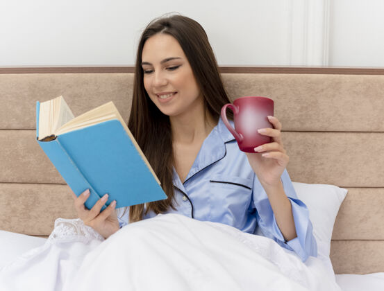 阅读穿着蓝色睡衣躺在床上的年轻漂亮女人卧室躺着周末