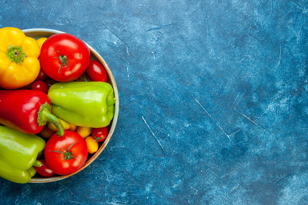 西红柿顶视图蔬菜樱桃西红柿Cumat不同颜色甜椒西红柿木盘上的蓝色桌子上的免费空间顶部甜椒樱桃