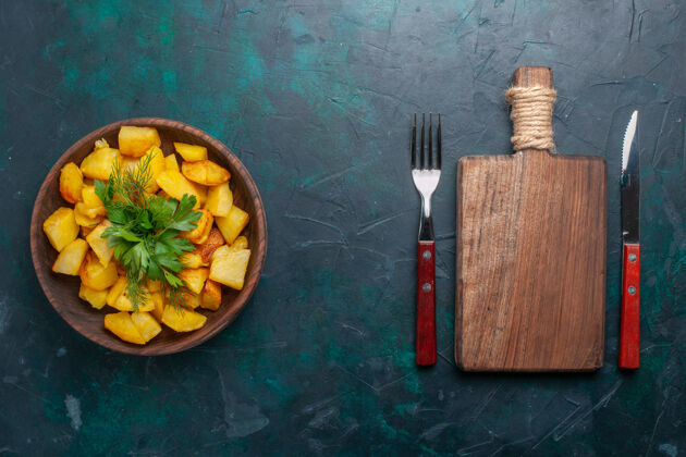 蔬菜俯视图深蓝色桌子上棕色盘子里放着烤土豆片和绿色蔬菜的美味一餐美味桌子健康