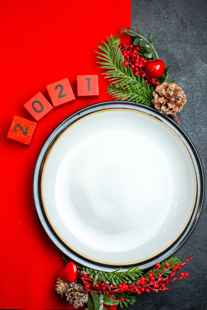 餐盘新年背景的垂直视图 带有餐盘装饰配件杉木树枝和数字 放在黑色桌子上的红色餐巾上圣诞节杯子盘子