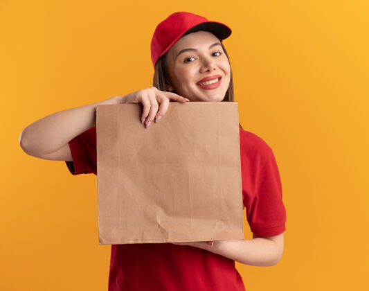 包装身着制服的微笑漂亮的送货员拿着纸包裹 隔离在橙色的墙上 留有复印空间微笑制服漂亮