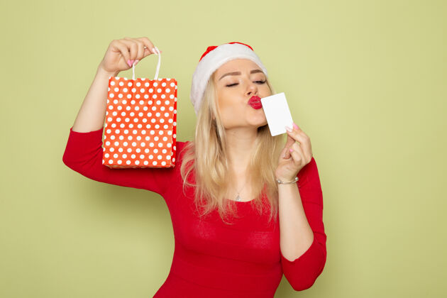银行正面风景美丽的女性手持礼物在小包装和银行卡上的绿色墙壁雪情感节日圣诞新年的颜色包装漂亮雪
