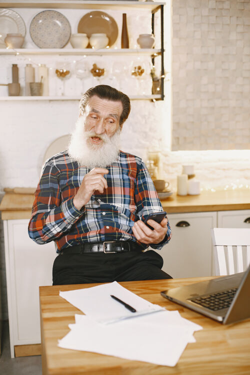 眼镜老人拿着笔记本电脑爷爷坐在圣诞装饰品里老人拿着手机坐着互联网办公室