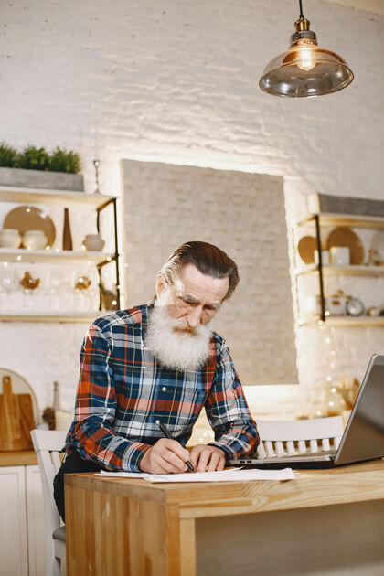 桌子老人拿着笔记本电脑爷爷坐在圣诞装饰品里早晨休闲工作