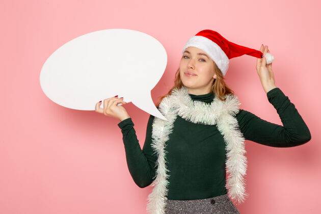 年轻的女性正面图年轻女性手持白色大招牌 微笑在粉色墙上圣诞新年造型节日色彩感慨圣诞高大色彩