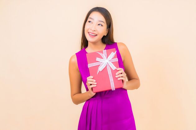 举行肖像美丽的亚洲年轻女子与红色礼品盒的颜色隔离的背景喜悦年轻人周年纪念