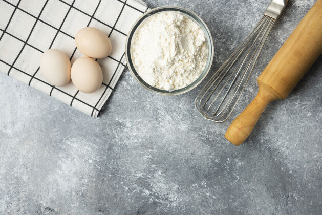 胡须一碗面粉 鸡蛋和厨房工具放在大理石表面上工具做的桌布