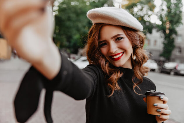 年轻情绪激动的白种女人在秋天喝茶时自拍高兴的姜姑娘戴着贝雷帽享受十月的日子户外自拍贝雷帽
