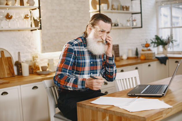 家庭老人拿着笔记本电脑爷爷坐在圣诞装饰品里老人拿着手机互联网桌子肖像