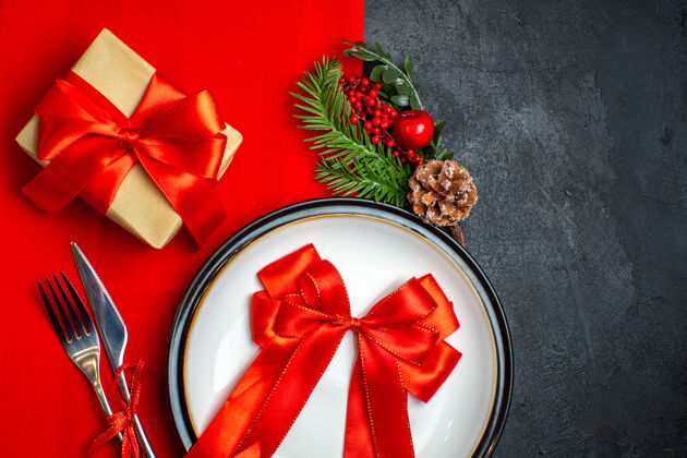 圣诞新年背景顶视图用红丝带放在餐盘上餐具套装装饰配件杉木树枝旁边的一个礼物上 一张红色餐巾放在一张黑色的桌子上风景餐巾树枝